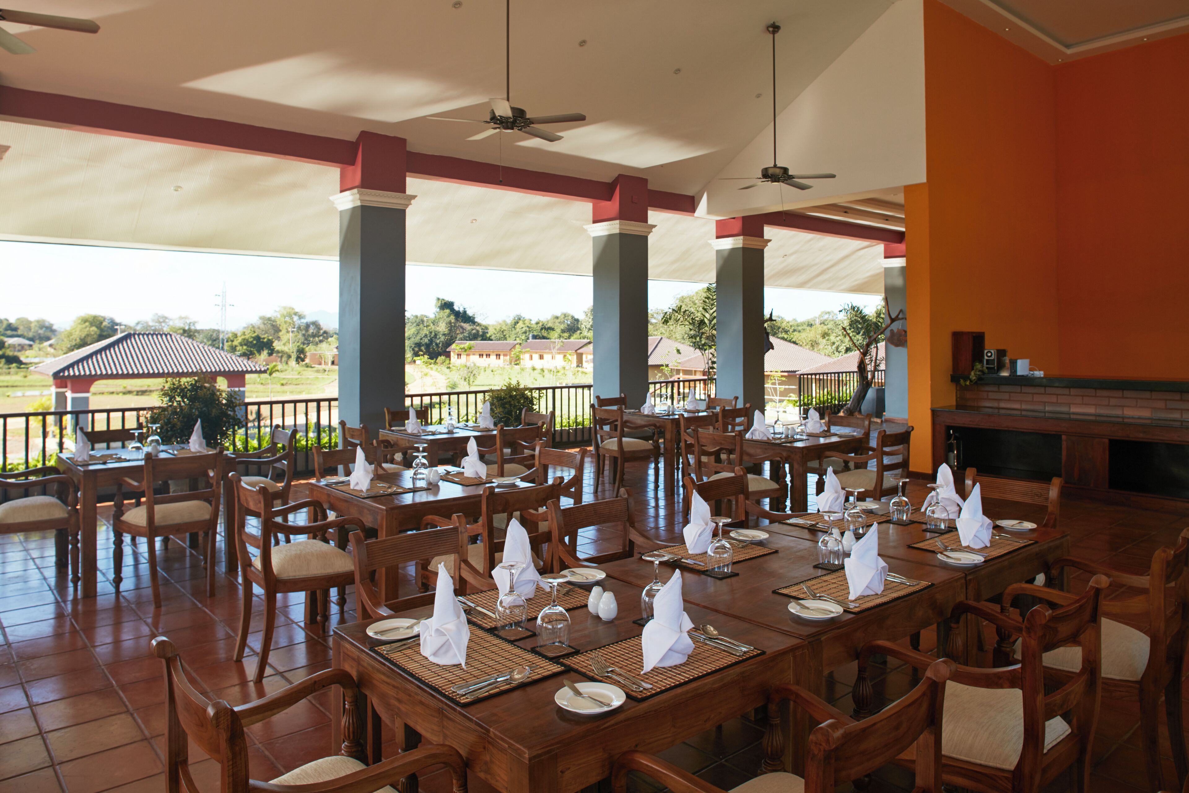 Un restaurant avec des tables et des chaises en bois, un espace extérieur couvert et une vue sur des bâtiments situés au loin.