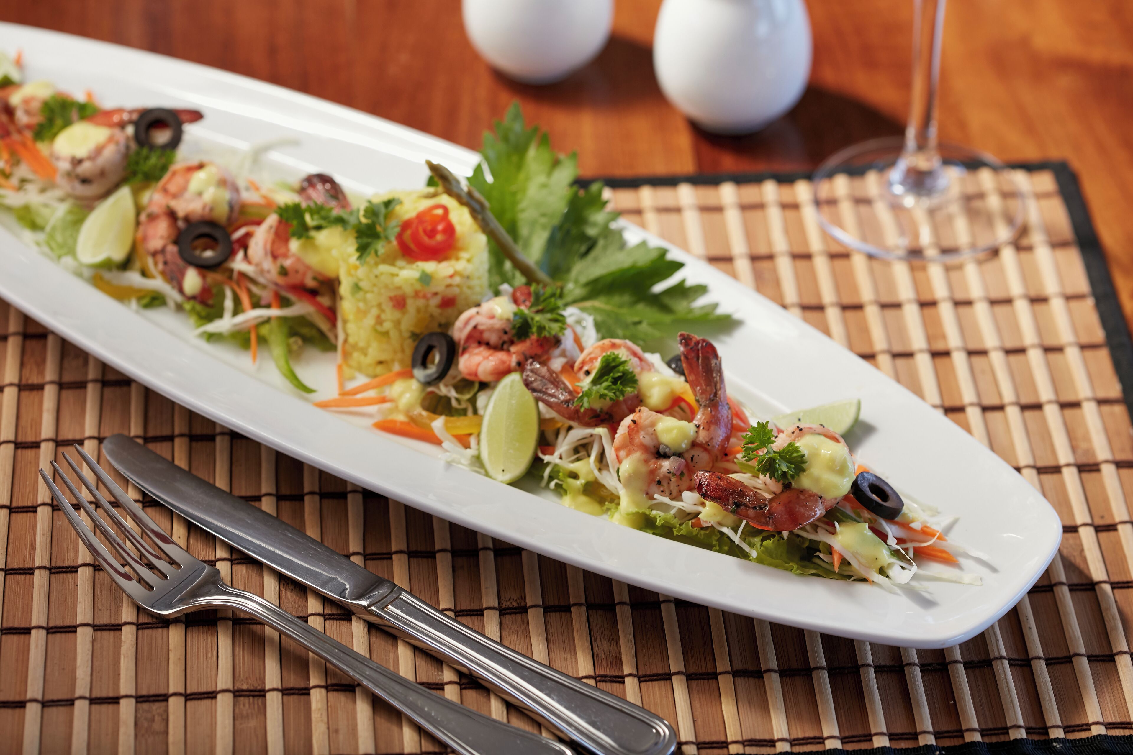 A white rectangular plate with a seafood salad, garnished with black olives, parsley, and a lime wedge.