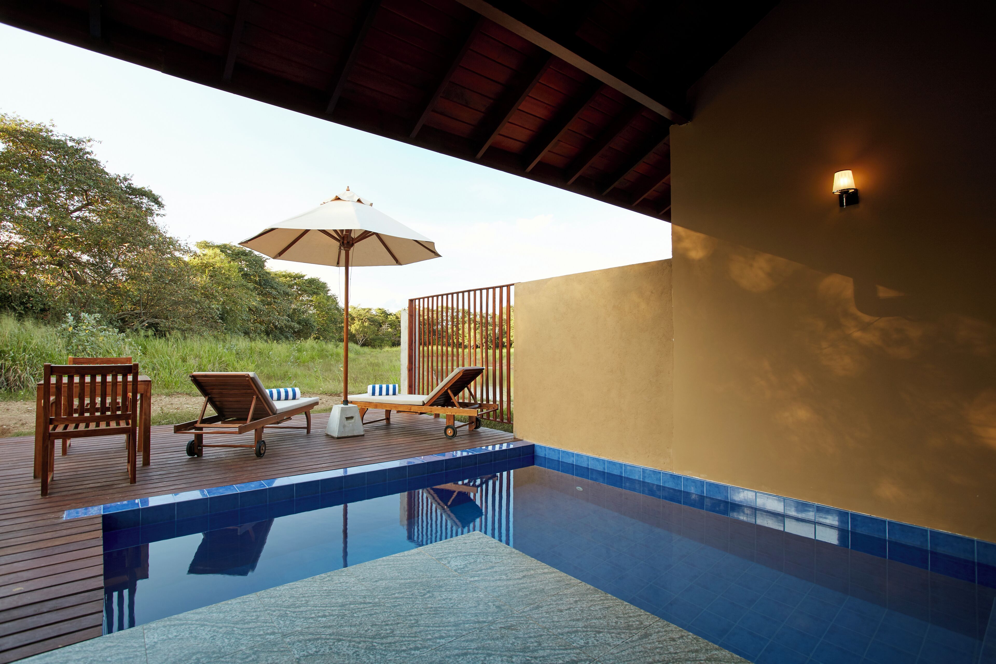 Un área junto a la piscina con terraza de madera, sillas de descanso y una sombrilla.