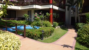 A hotel courtyard with a pool, lush greenery, and a red pillar. - Kalim Residence Unit - 215 (Patong)