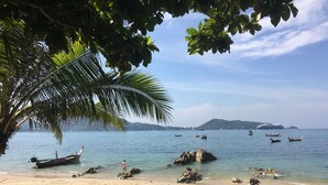 A beach with clear water, boats, and a large ship in the distance. - Kalim Residence Unit - 215 (Patong)