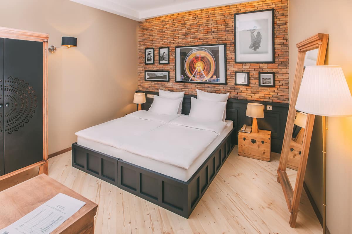 A bedroom with a brick-patterned wall, a bed with white bedding, two bedside tables with lamps, and a wooden dresser.
