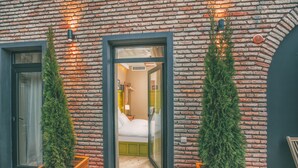 A hotel room with a brick exterior, wooden planter boxes with greenery, and a visible bed with a green headboard. - Kisi Boutique Hotel (Tbilisi)