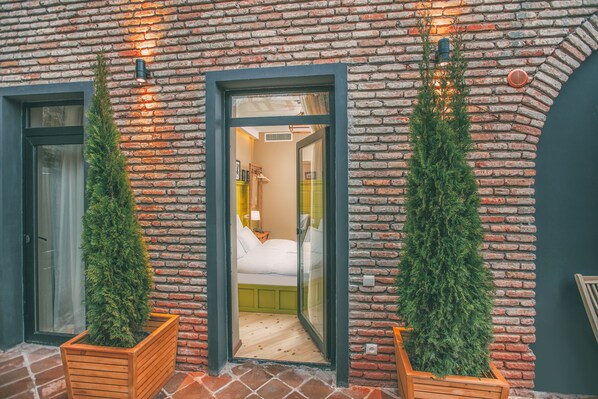 A hotel room with a brick exterior, wooden planter boxes with greenery, and a visible bed with a green headboard.