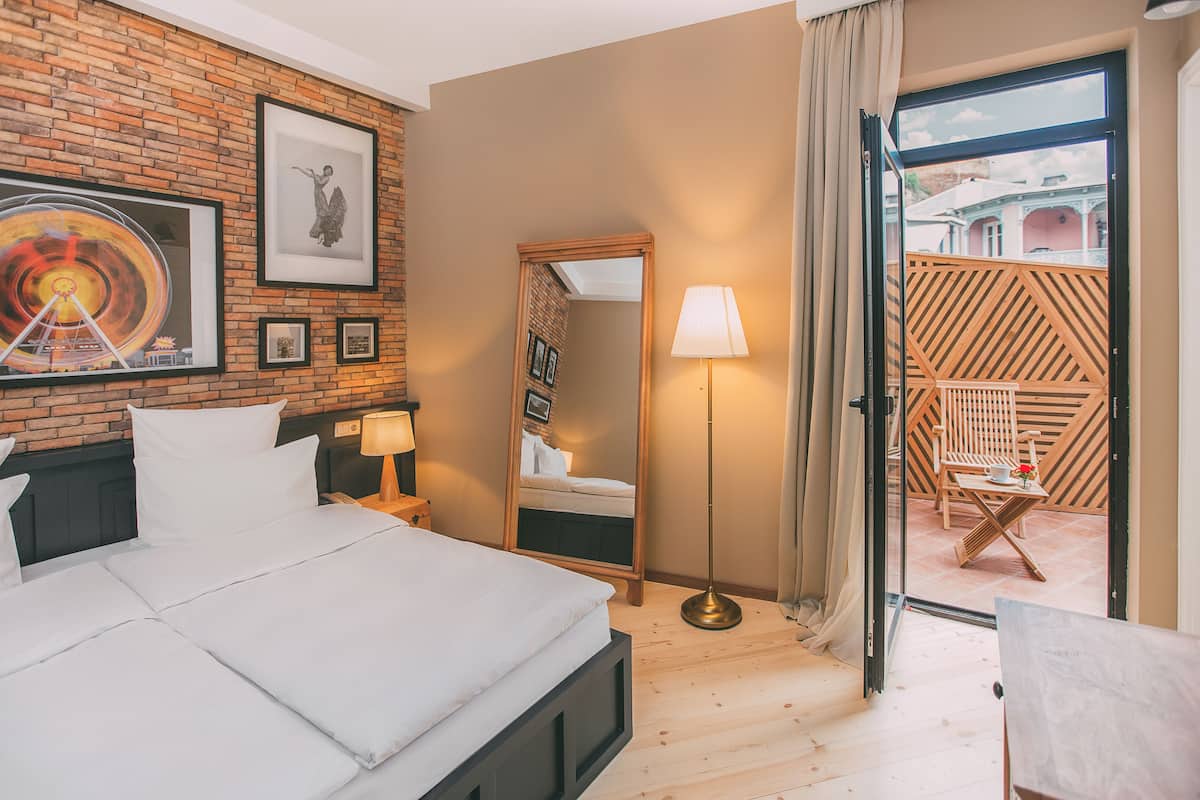 A hotel room with a bed, a mirror, a lamp, and a view of the outside balcony.
