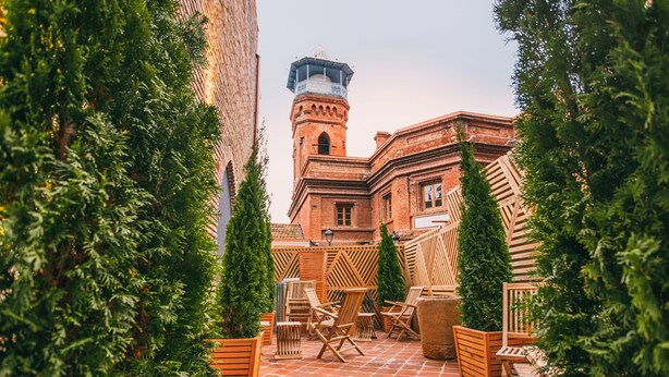 A courtyard with brick flooring, wooden furniture, and green plants. - Kisi Boutique Hotel (Tbilisi)