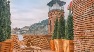 Una terraza con mobiliario de madera, un muro de ladrillo y una torre al fondo.