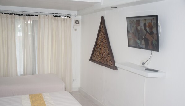 Un dormitorio con una cama, un televisor montado en la pared y un ventanal con cortinas.