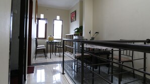 A dining area with a long table and chairs, a small kitchen area, and a view of the outside through a window. - Unique Guesthouse (Bandung)