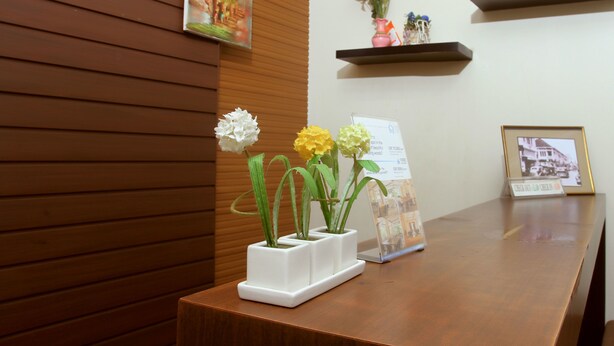 A reception desk with a wooden panel wall, a framed picture, a small shelf with decorative items, and a signboard. - Unique Guesthouse (Bandung)