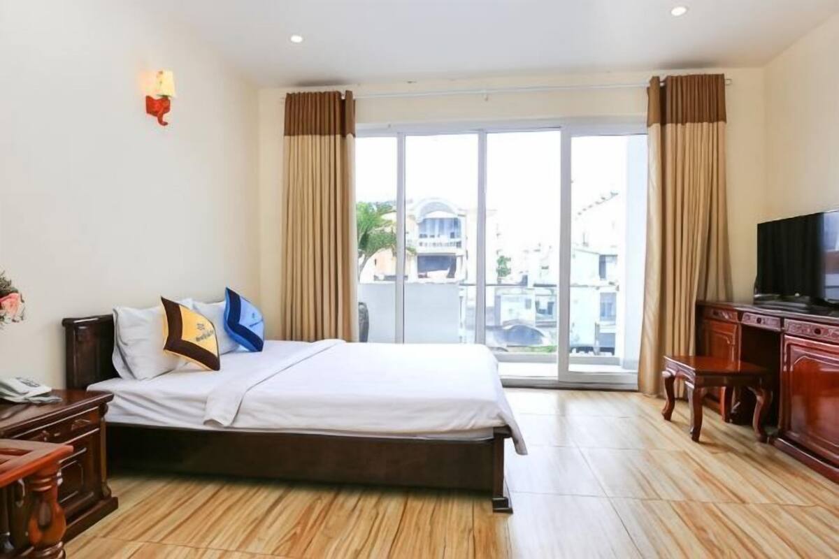 A hotel room with a bed, a desk, a television, and a sliding glass door to the outside.