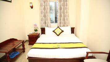 A neatly made bed with a yellow and black bedspread, a wooden nightstand with a lamp, a wooden bench, and a chair.