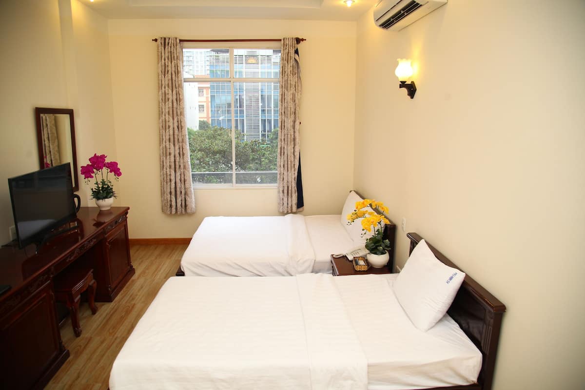 A hotel room with two beds, a TV, a desk, and a window with curtains.