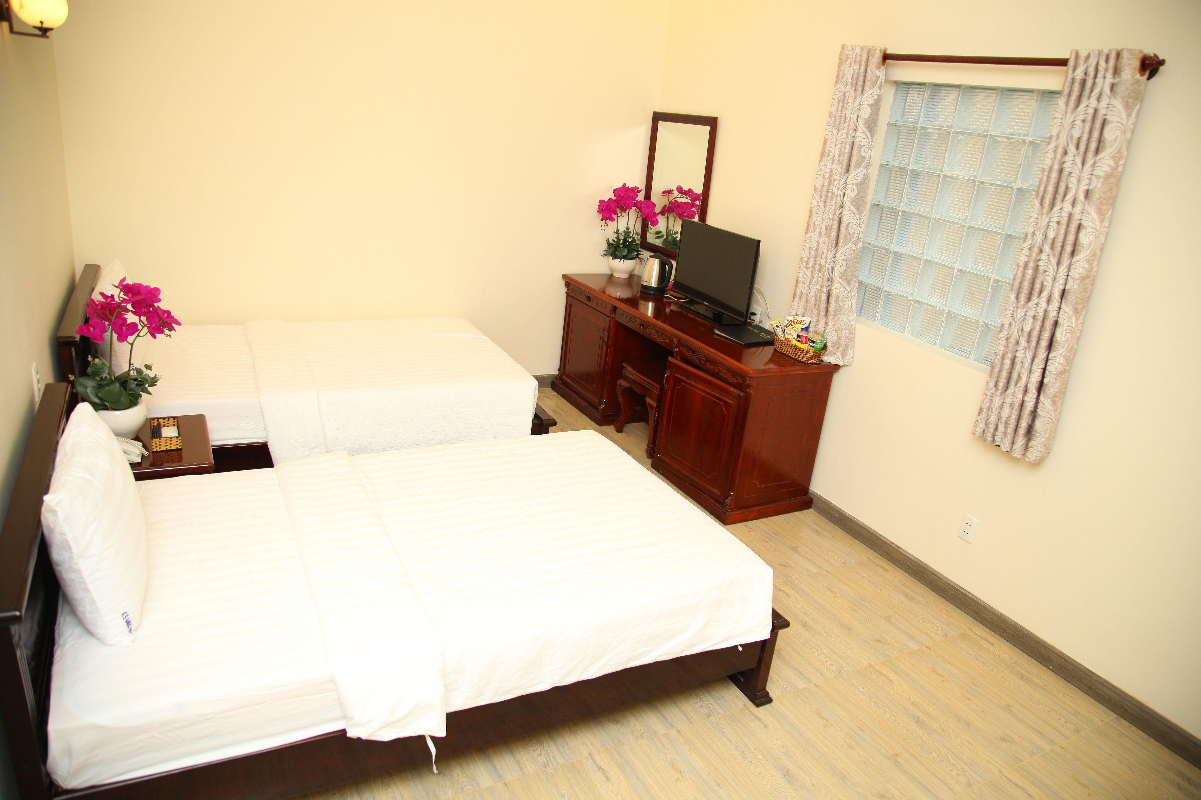 A hotel room with two single beds, a wooden dresser, a television, and a window with curtains.