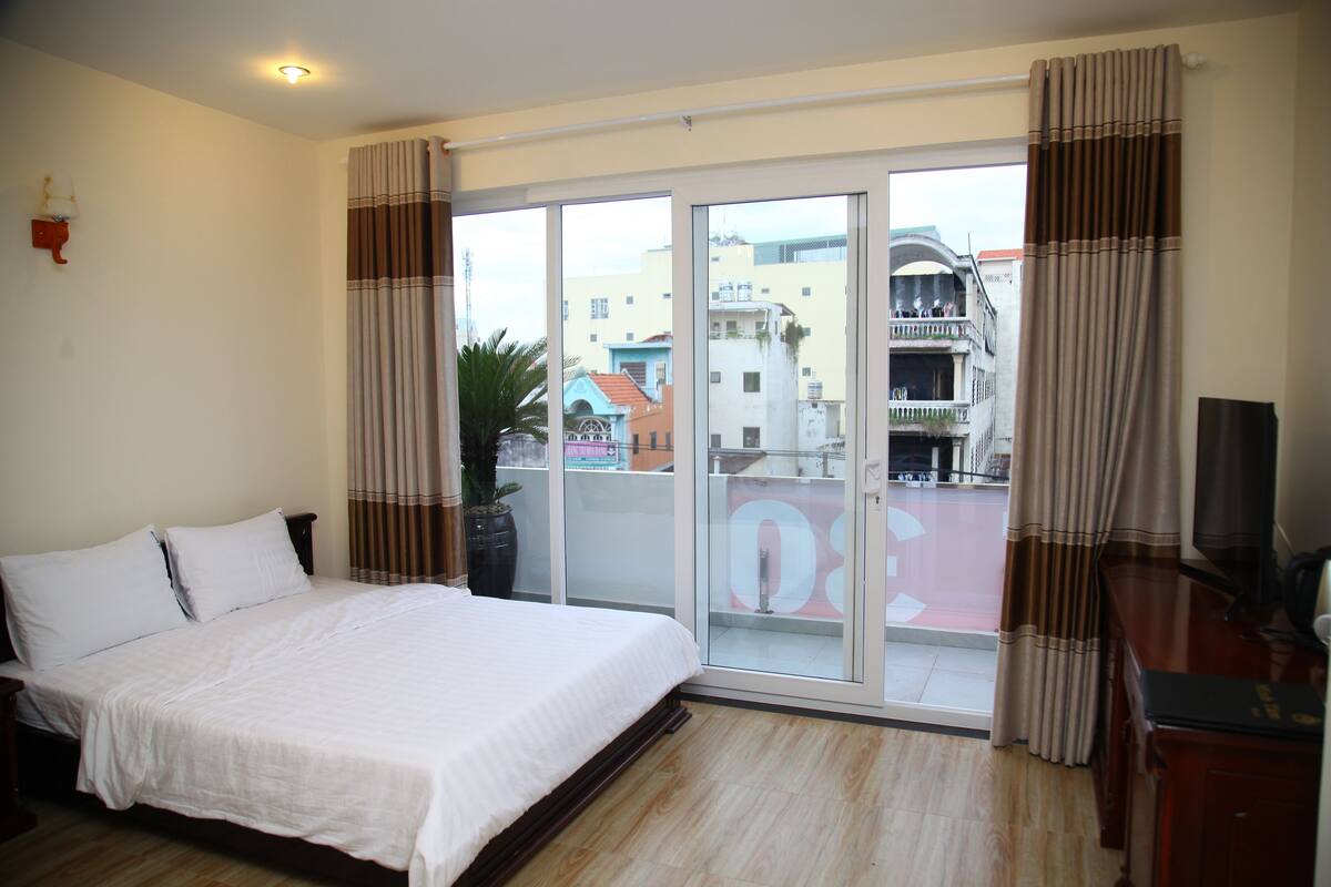 A hotel room with a large bed, sliding glass doors to a balcony, and a view of the cityscape.