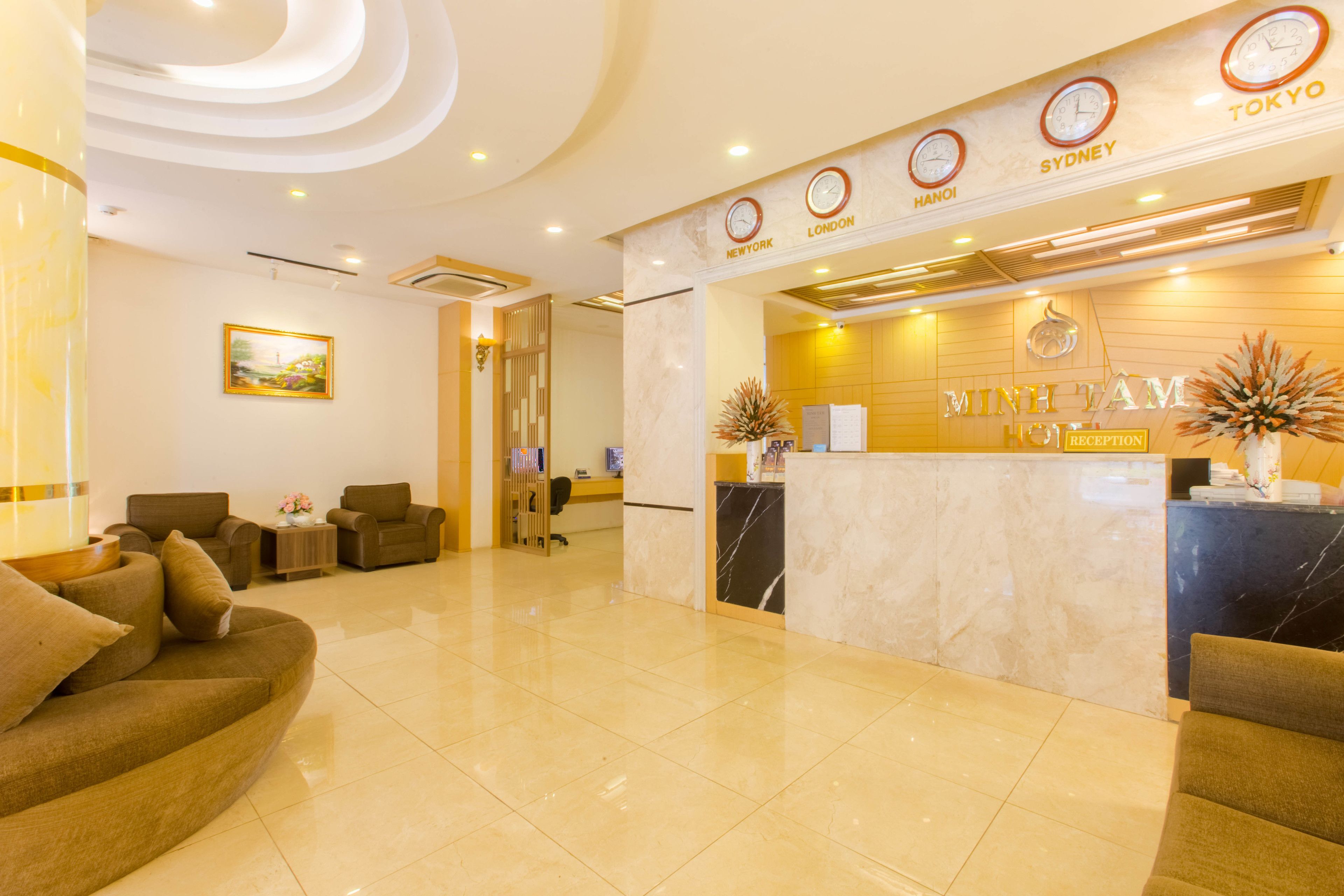 A hotel reception area with a marble reception desk, a clock displaying time in multiple cities, and a seating area with sofas.