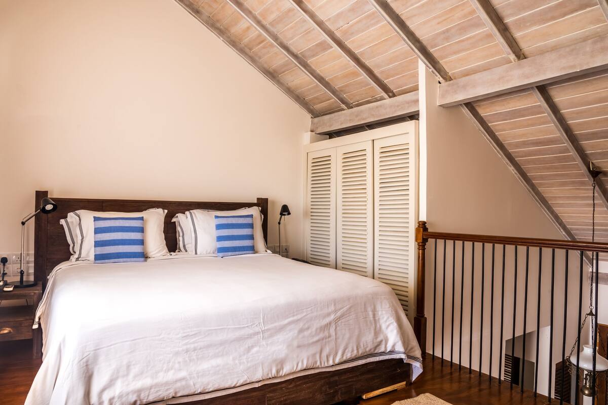 A bedroom with a wooden bed frame, white bedding, and a sloped ceiling.