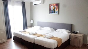 Hotellihuone, jossa on parivuode, yöpöytä lampun kanssa, pieni puinen kaappi ja taulu seinällä.