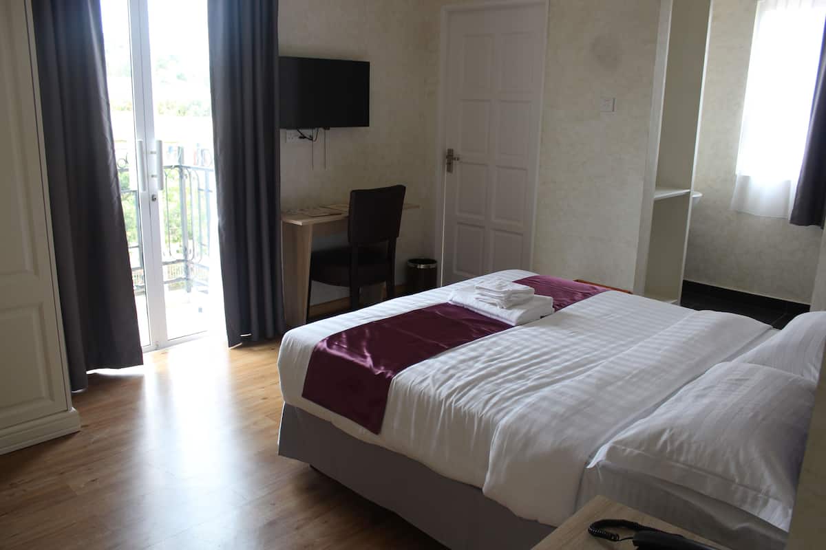 A hotel room with a bed, a desk, a chair, and a TV mounted on the wall.