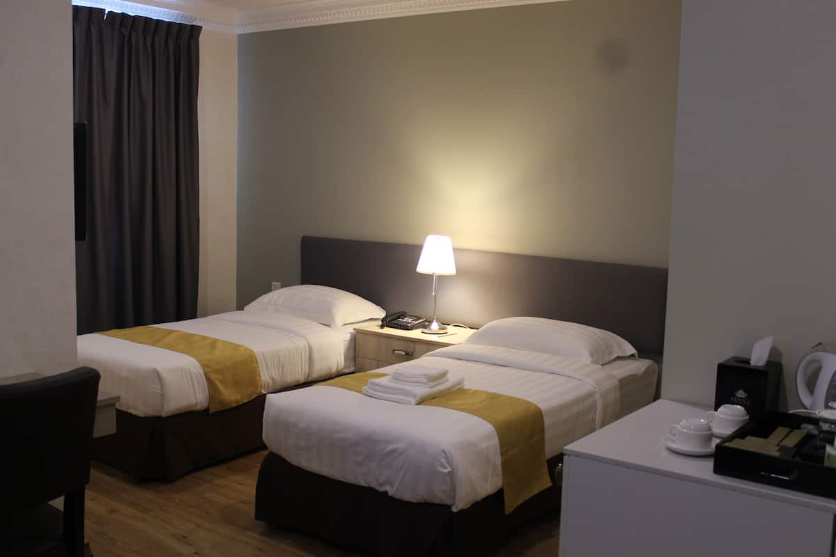 A hotel room with two beds, a desk, a lamp, a telephone, and a coffee maker.