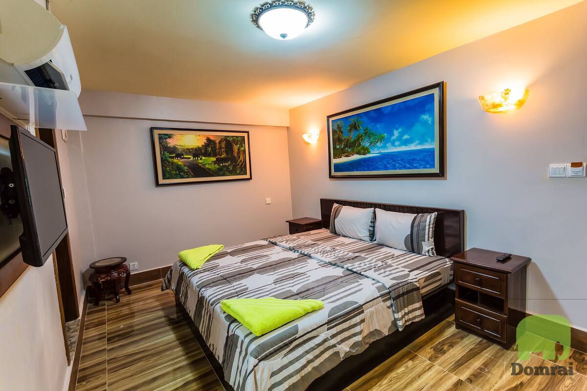 A bedroom with a bed, nightstands, a TV, and two wall-mounted lights.