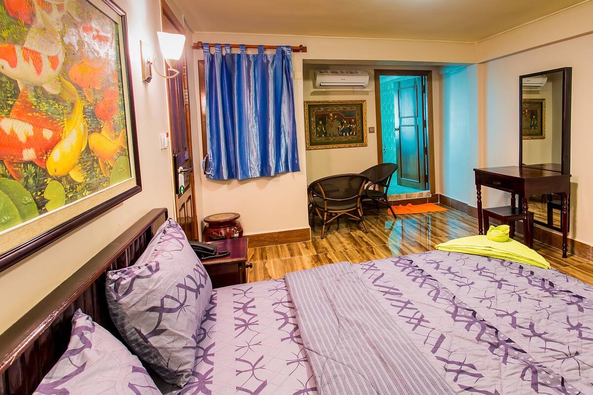 A hotel room with a bed, a chair, a desk, a painting, and a curtain.