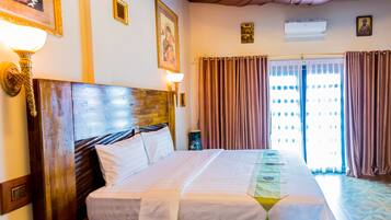 A hotel room with a large bed, a wooden headboard, a wall-mounted lamp, and a window with curtains.