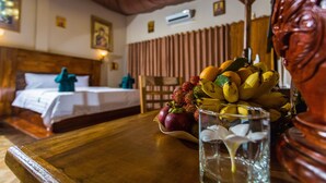 Une chambre d’hôtel avec un lit en bois, une table de chevet sur laquelle se trouve un panier de fruits, un vase avec des fleurs et une sculpture décorative en bois.