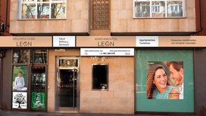 A building with a wellness clinic and apartments. There are signs for 'Wellness Clinic Leon' and 'Apartamentos Leon'. The entrance has a glass door and a small window. - Apartamentos Leon (León)