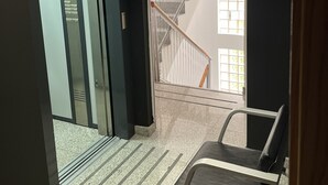 An interior view of a hotel lobby with a reception desk, a staircase, and an elevator. - Apartamentos Leon (León)