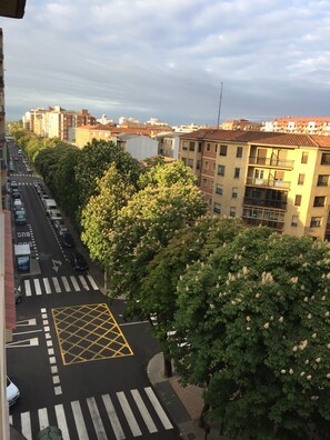 A street view with a pedestrian crossing, parked cars, and buildings in the background. - Apartamentos Leon (León)