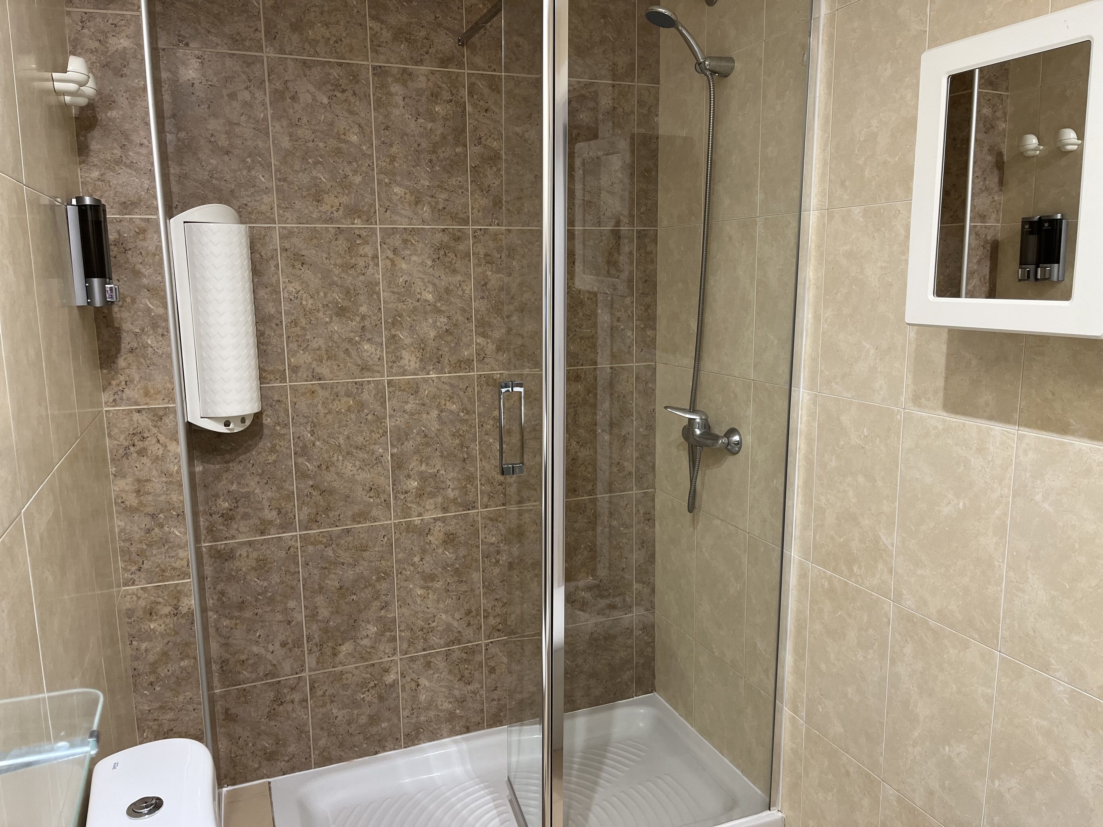 Un área de ducha moderna con puerta de vidrio, cabezal de ducha manual y dispensador de toallas.