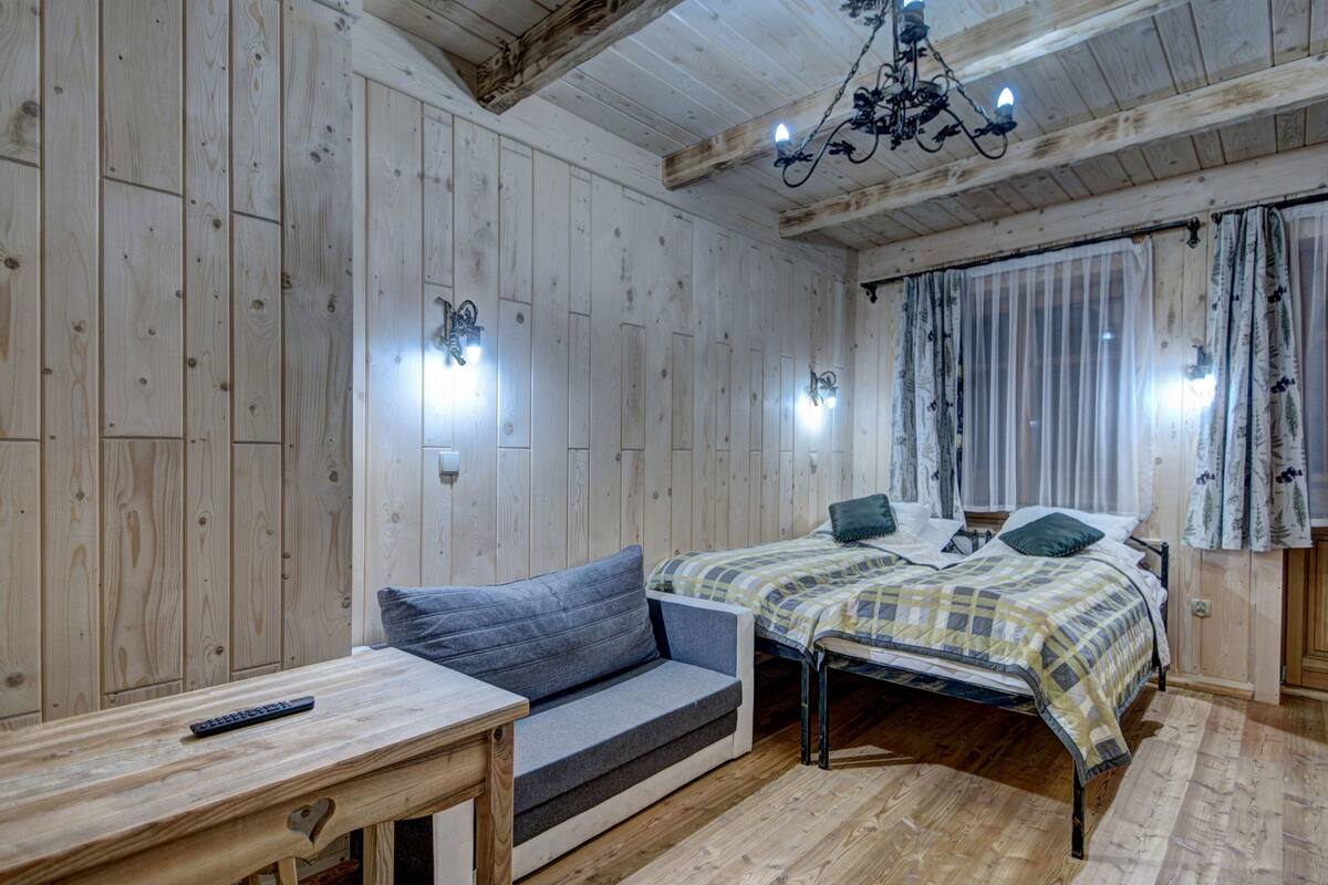 Una habitación con paneles de madera, con una cama, un sofá, una mesa y una araña.