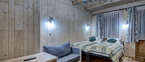 A wooden-paneled room with a bed, a sofa, a table, and a chandelier.