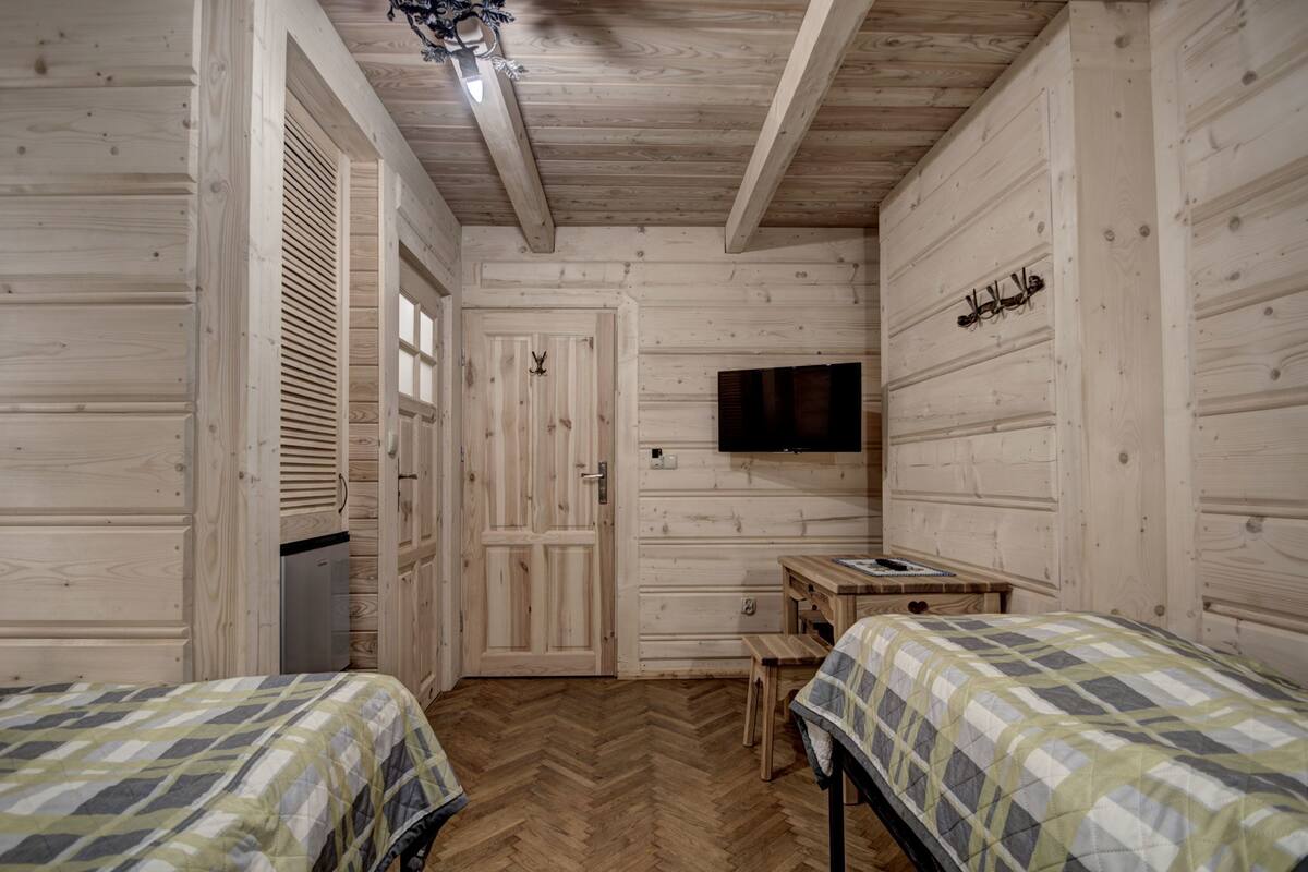Una habitación con paneles de madera, dos camas, un escritorio, un televisor y una puerta.