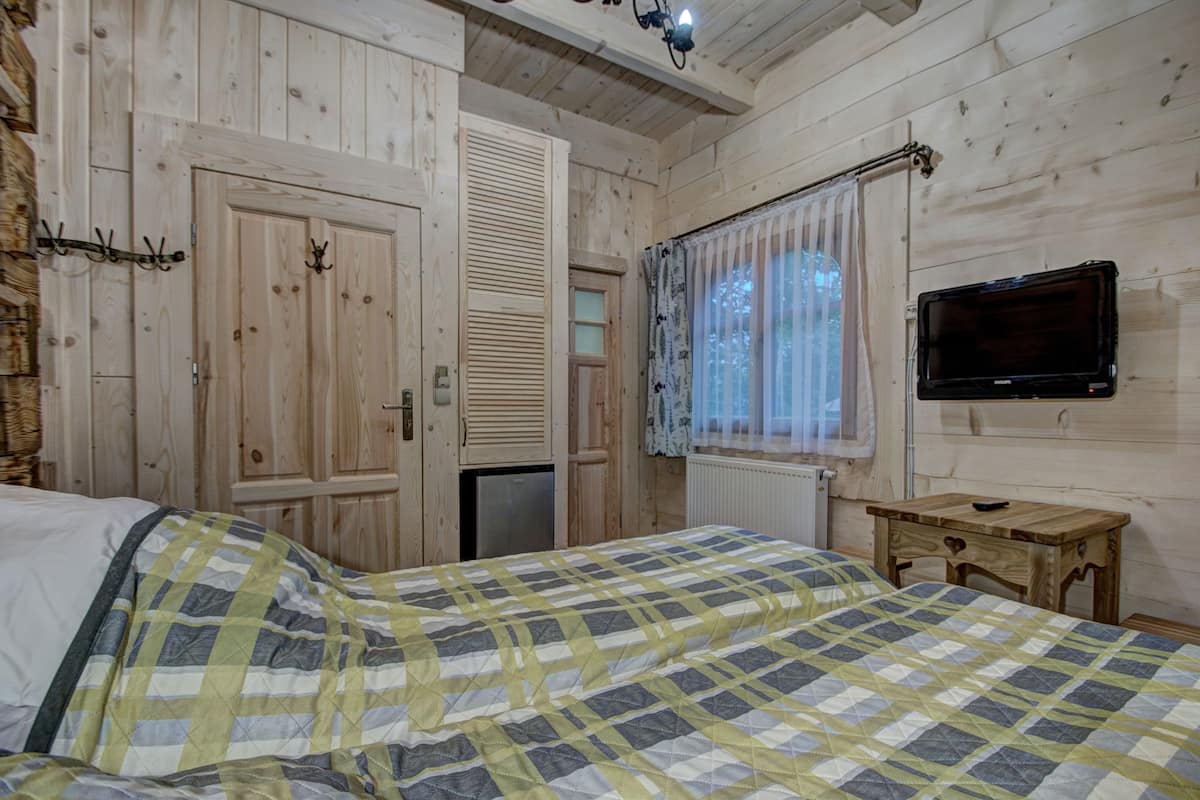 Una habitación de madera con una cama, un televisor y un ventanal con cortinas.