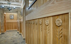 A wooden wall with carved floral and leaf patterns, a chandelier, and a stone floor. - Pokoje Gościnne Światłomir (Zakopane)