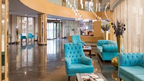 Um lobby amplo com uma parede curva de madeira, uma área de estar com poltronas estofadas em azul e um lustre decorativo.