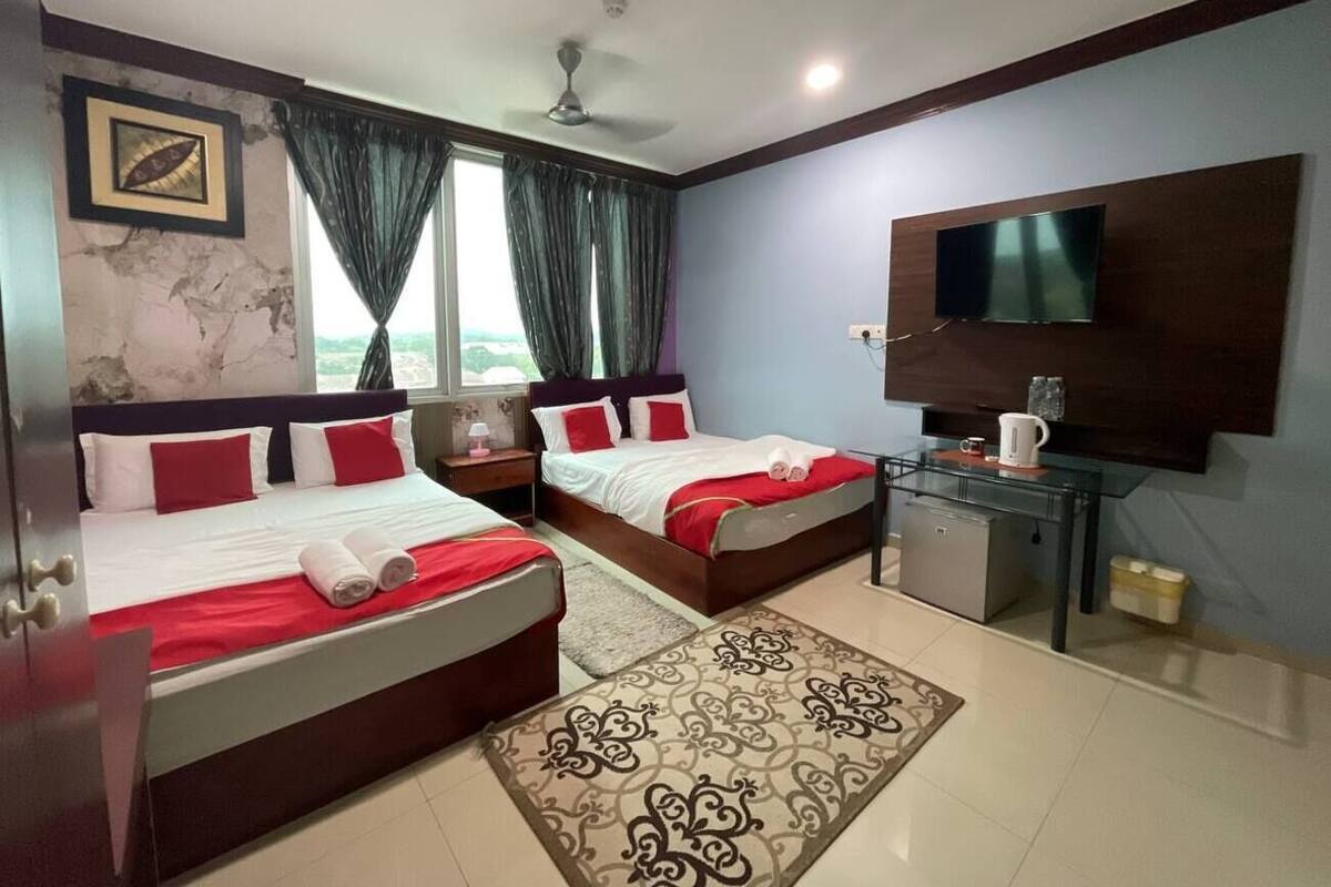 Une chambre d’hôtel avec deux lits, une télévision, une petite kitchenette et une fenêtre avec des rideaux.