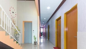 Un couloir d’hôtel avec un escalier, une plante en pot et des portes donnant sur les chambres.