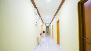Un long couloir étroit, avec des portes de chaque côté, une petite table avec une chaise, et un extincteur sur le mur de gauche.