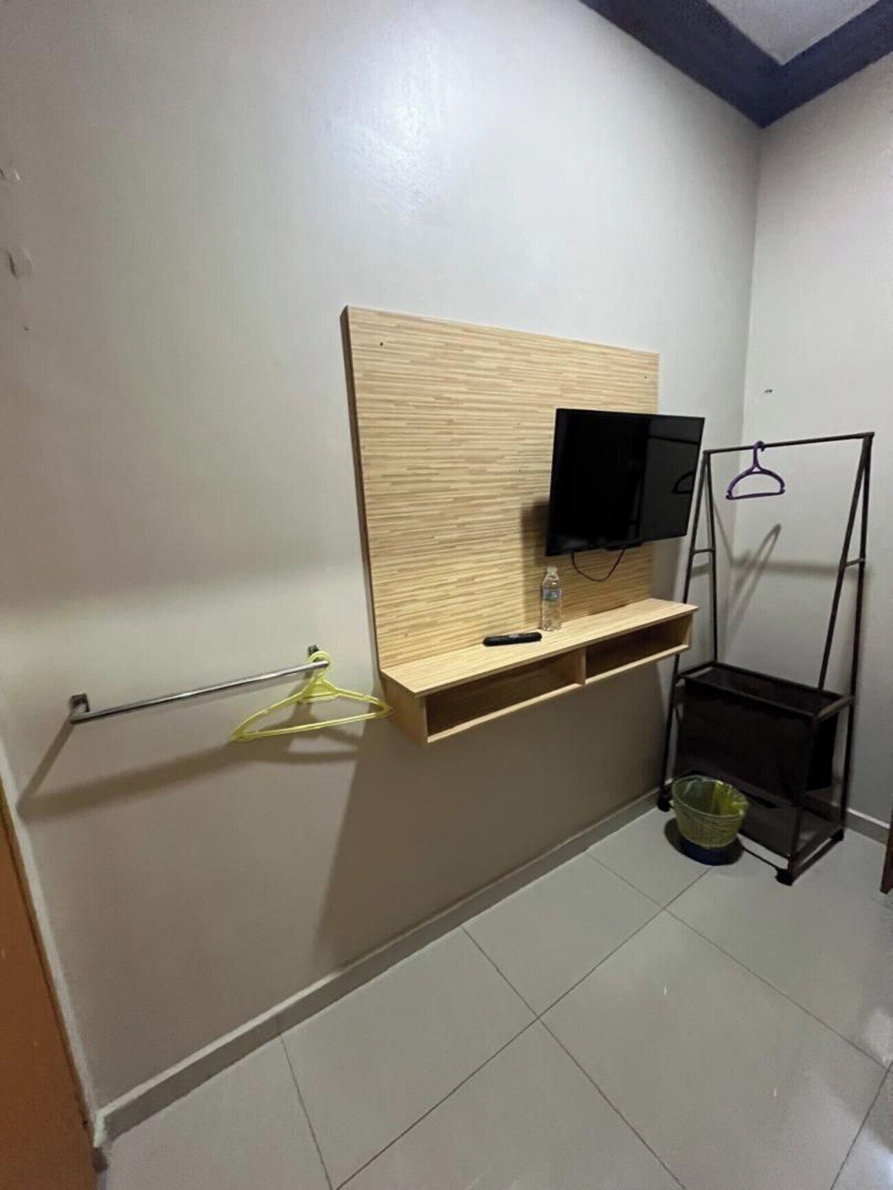 Une salle de bain avec un meuble-lavabo en bois, un téléviseur fixé au mur, un porte-serviettes et une petite étagère.