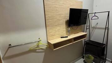 Une salle de bain avec un meuble-lavabo en bois, un téléviseur fixé au mur, un porte-serviettes et une petite étagère.