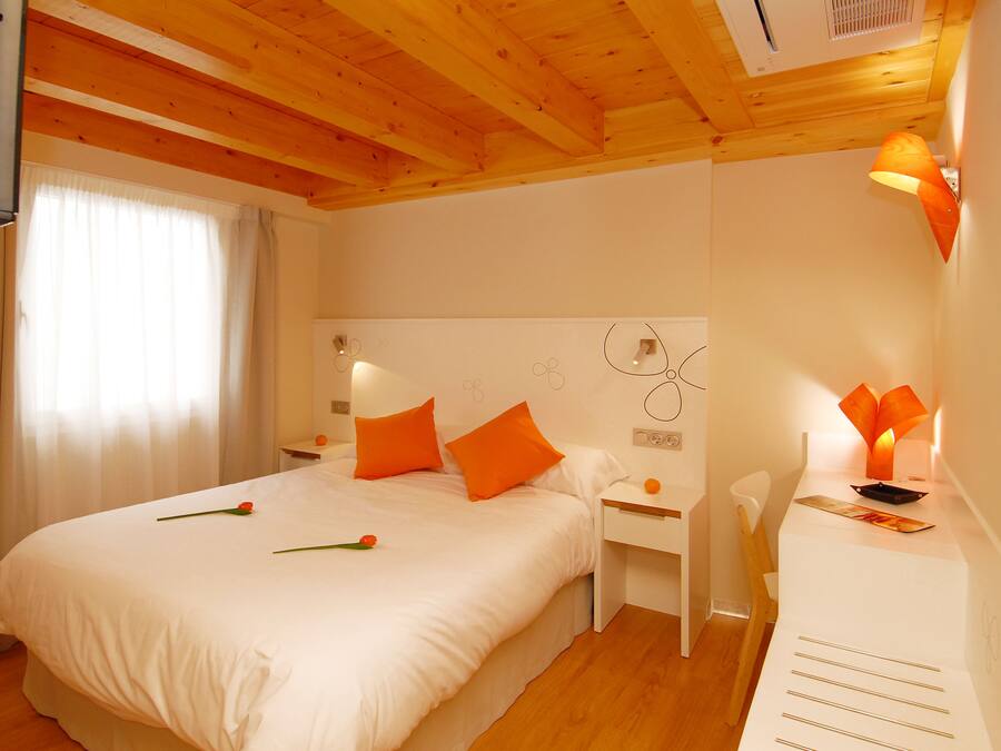 Un dormitorio con una cama grande, paredes blancas, vigas de madera en el techo y dos mesitas de noche con lámparas.