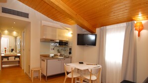A modern kitchen with white cabinets, a microwave, and a flat-screen TV. There is a dining area with a white table and chairs, and a black sofa in the living room. - Hostal riMboMbin (Burgos)