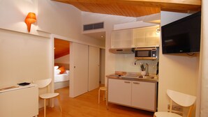 A compact kitchen with a microwave, stove, and sink, a small dining area with two chairs, and a TV mounted on the wall. - Hostal riMboMbin (Burgos)