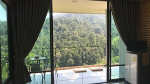 A room with a large sliding glass door leading to a balcony with a view of a forested hillside.