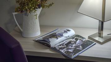 Un bureau sur lequel se trouve un vase blanc contenant des fleurs, une lampe et un magazine ouvert.