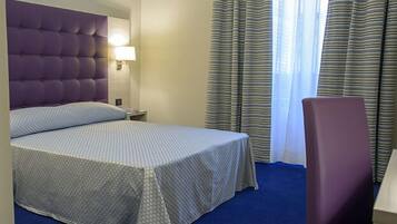 A hotel room with a bed, a nightstand, a lamp, a chair, and a window with curtains.