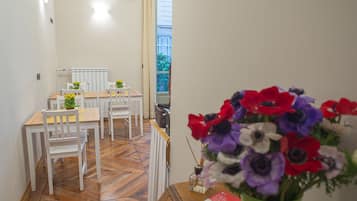 Un coin repas avec une table en bois et des chaises blanches, un radiateur et une fenêtre donnant sur un paysage verdoyant.